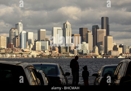 Cloud covered waterfront Seattle skyline from Washington State Ferry showing silhouette of father son between cars in foreground Stock Photo