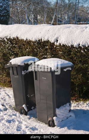 Two domestic waste bins awaiting collection during the winter after snowfall Stock Photo