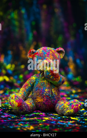 Teddy bear sat on a black cloth covered in coloured powder. Still life Stock Photo