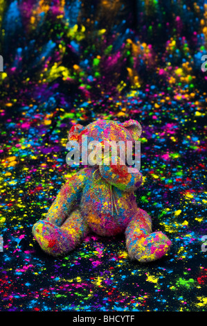 Teddy bear sat on a black cloth covered in coloured powder. Still life Stock Photo