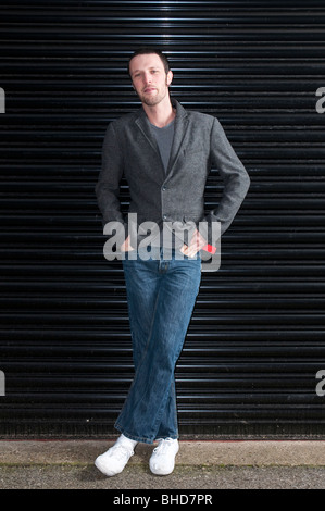 Portrait of a young man smiling dressed casually leaning against uniform dark background. Stock Photo