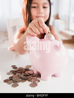 Mixed race girl putting coin in piggy bank Stock Photo