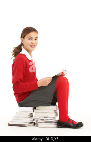 Female Student In Uniform Sitting On Pile Of Books Reading Stock Photo