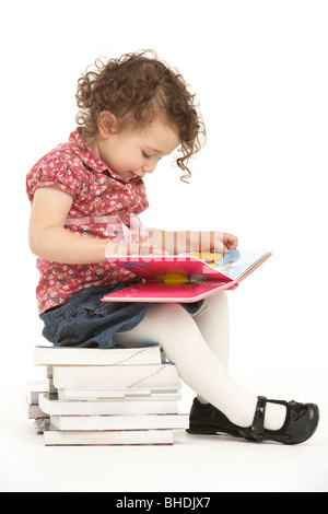 Young Girl Sitting On Pile Of Books Reading Stock Photo