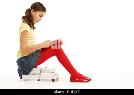 Young Girl Sitting On Pile Of Books Reading Stock Photo