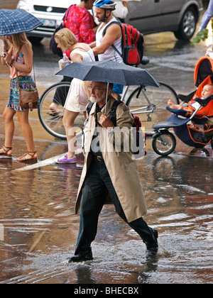 MAN HOLDING UMBRELLA AND WALKING THROUGH PUDDLE IN ROAD  ON SWANSTONE STREET MELBOURNE VICTORIA  AUSTRALIA Stock Photo