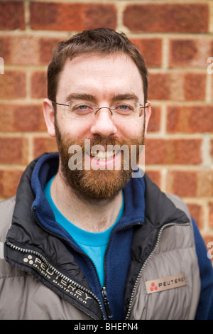 A bearded man smiles in front of a brick wall. Stock Photo