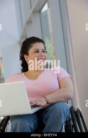 Close-up of a woman sitting in a wheelchair and using a laptop Stock Photo