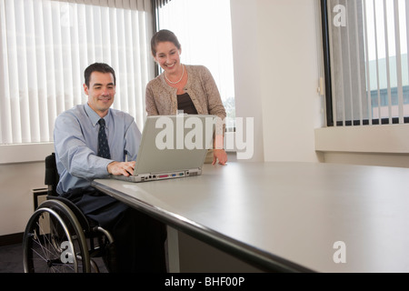Secretary standing beside a handicapped businessman working on a laptop Stock Photo