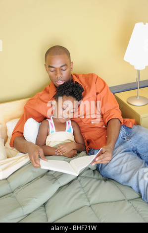 Black father reading book to daughter in bedroom Stock Photo