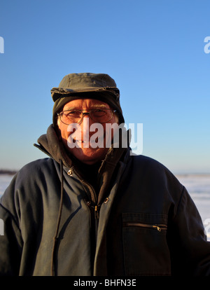 Old fisherman dressed in winter clothes along frozen Miramichi Bay with cap on in New Brunswick Canada Stock Photo
