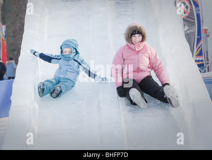 A woman and her daughter ride an ice slide at the Quebec Winter Carnival (Carnaval de Quebec) in Quebec city. Stock Photo