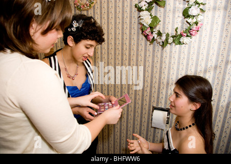 Preparing for their Formal Dance, five multi-ethnic girls putting on make up and doing their hair in the bathroom. Stock Photo