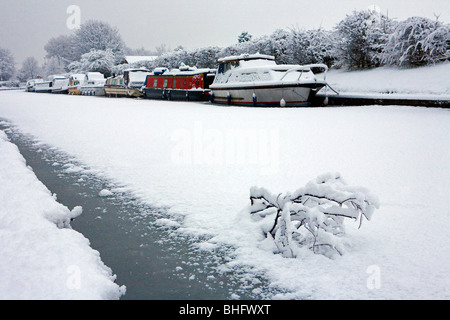 Boats frozen into their moorings with snow covering the iced up Bridgewater canal and a snow covered branch in the foreground Stock Photo