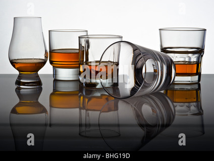 Play of light and colours in glasses for whisky with reflexion. One glass lies on one side in others whisky is poured.