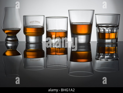 Five glasses with alcohol stand on glass. All glasses are reflected in glass of grey colour Stock Photo