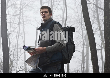 A young male hiker holding a map in a misty forest Stock Photo
