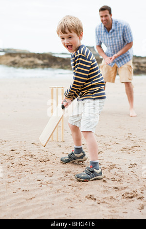 Father and son playing cricket on beach