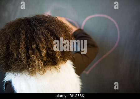 Girl drawing heart on blackboard Stock Photo