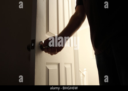 Man's hand opening a door to a dark room at night Stock Photo