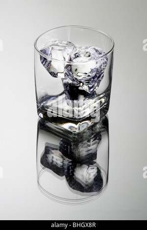 Empty glass tumbler with ice cubes on gray background with reflection Stock Photo