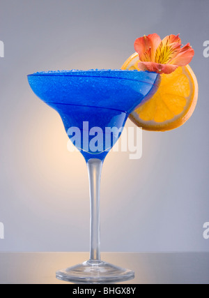 Blue Hawaiian mixed drink with orchid and orange garnish on plain background Stock Photo