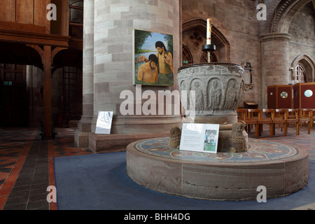 Set upon a circular plinth,the stone carved Font at Hereford Cathedral set against a picture of a Baptism hung on a huge column. Stock Photo