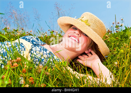 Young teenage girl laying on summer meadow amid wildflowers in straw hat Stock Photo