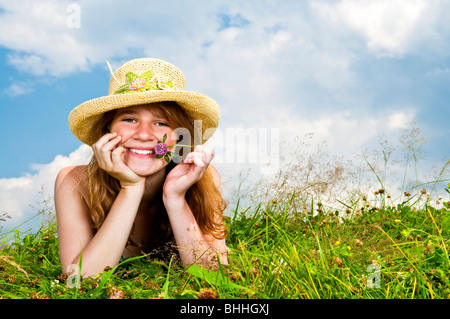 Young teenage girl laying in summer meadow resting chin on hand holding flower Stock Photo