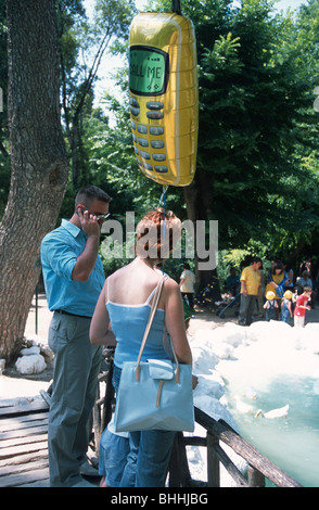 A couple - one talking on a mobile phone and the other with a mobile phone balloon: 'CALL ME'.  Athens, Greece. Stock Photo