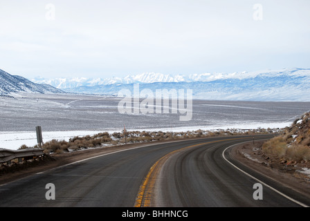 long paved and winding road with snow in landscape Stock Photo