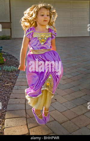 Happily dressed up in fancy clothes, a three year old blond girl jumps for joy outside her home in Southern California. Stock Photo