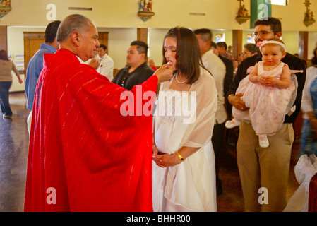 A priest offers communion at Mass to his mostly Hispanic parishioners in a Long Beach, California, Catholic church. Note pregnan Stock Photo