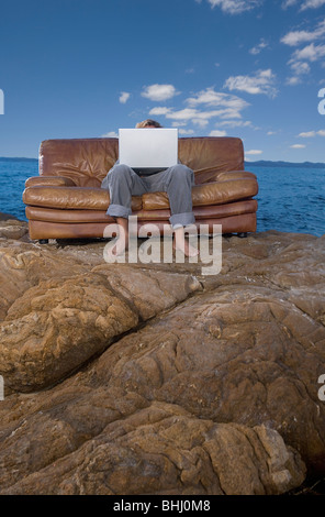 man on couch at beach with laptop Stock Photo