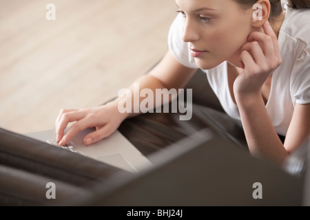 Young woman lies on leather sofa working on laptop