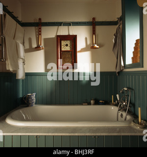 Wooden clock and candlesticks on peg-rail above bath in turquoise green paneled Shaker-style bathroom Stock Photo