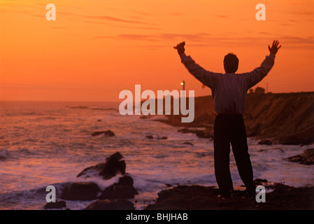 Businessman with raised arms and cell phone celebrating success and life near Point Arena Lighthouse on Central California coast Stock Photo