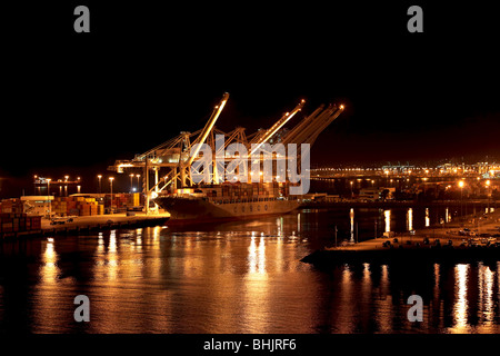 Chinese cargo ship in port of Long Beach California at night. Bright vibrant lights reflect off water. Stock Photo