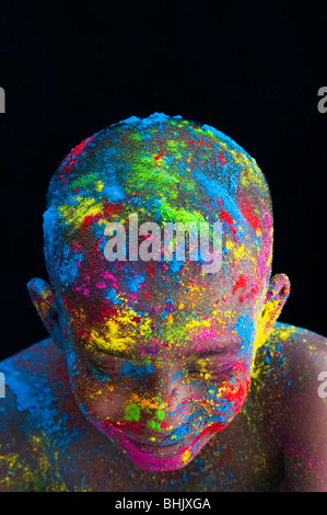 Happy young Indian boy covered in coloured powder pigment against a black background Stock Photo