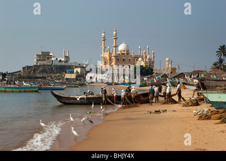 India, Kerala, Kovalam, Vizhinjam village fishermen unloading fishing boats on beach in front of mosque Stock Photo