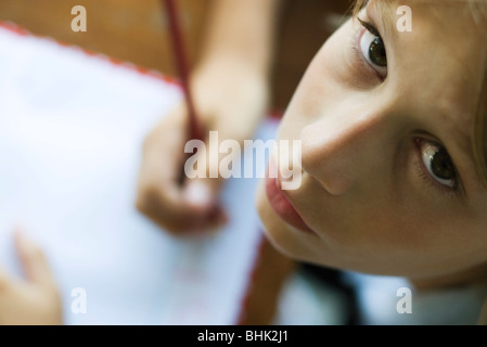 Boy writing in notebook, pausing work to look up at camera Stock Photo