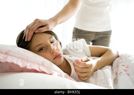 Girl checking temperature with thermometer, mother caressing forehead Stock Photo