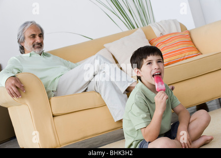 Boy eating popsicle, grandfather relaxing in background Stock Photo
