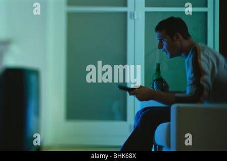 Man watching TV, holding beer and remote, side view Stock Photo