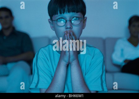 Boy watching TV with hands clasped over mouth Stock Photo