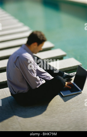 Businessman sitting on ground beside pool, using laptop computer Stock Photo