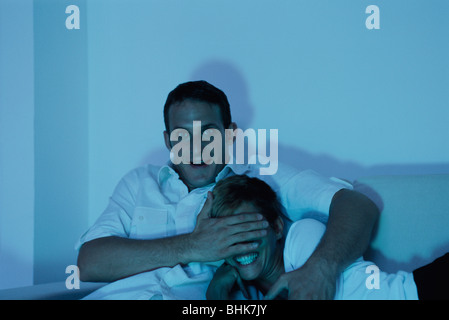 Couple watching TV together, man covering woman's eyes with his hand Stock Photo