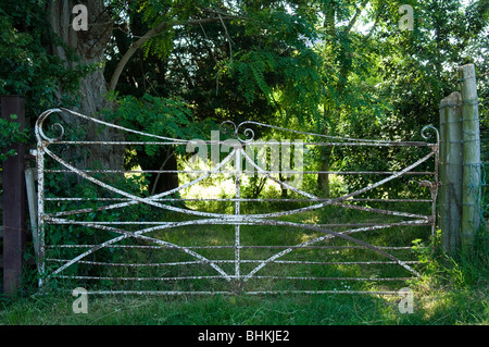 White metal ornamental gate leading to a small wood and then a meadow Stock Photo