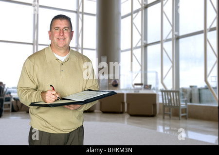 A mature business man wearing casual dress attire taking notes in a large lobby Stock Photo