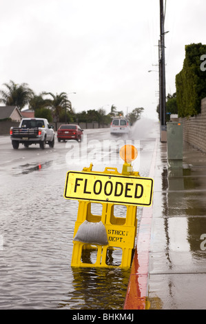 A car kicks up a pool of rainwater over a street flooded sign during bad, rainy weather. Stock Photo